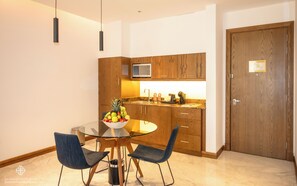 A modern kitchen with wooden cabinets, a microwave, and a glass dining table with chairs. - Jasmine Garden Hotel (Jeddah)