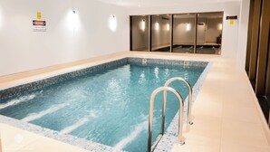 Una piscina con borde de azulejos, una escalera metálica y un muro de separación de vidrio.