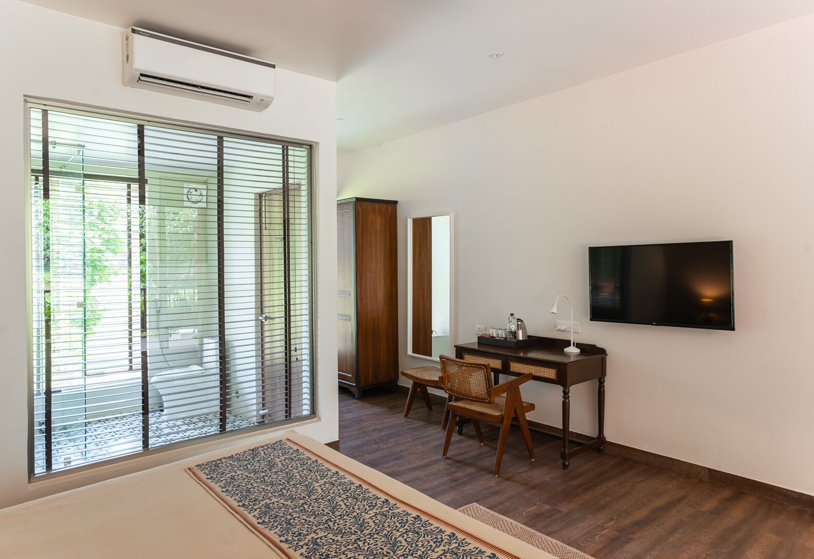 A modern room with a large sliding glass door, a flat-screen TV mounted on the wall, a wooden desk, and a chair.