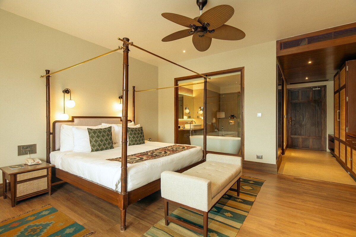 A four-poster bed with a canopy, a sitting area, a large mirror, and a wooden wardrobe.