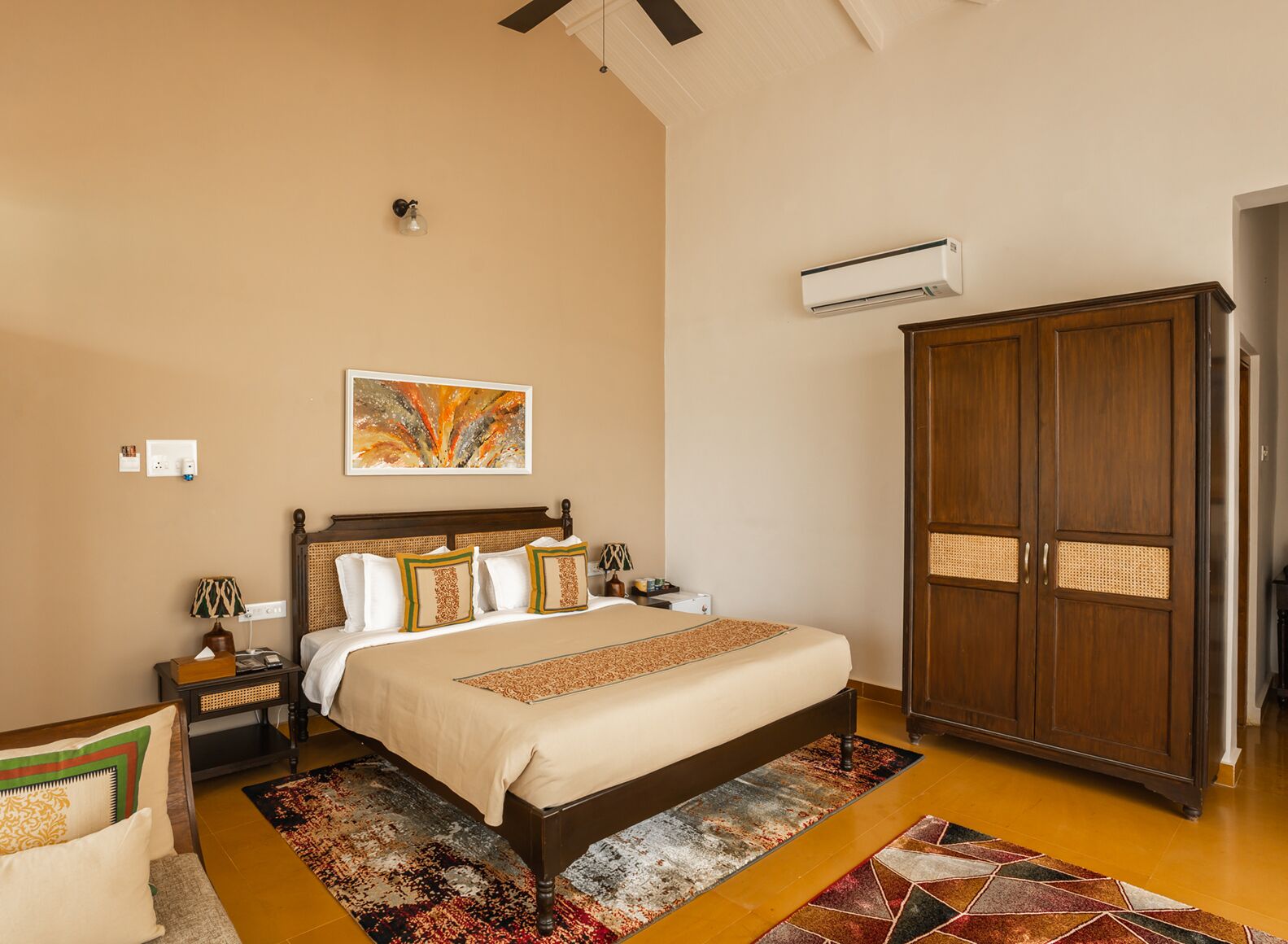 A bedroom with a bed, nightstands, a wardrobe, an air conditioner, and a wall-mounted artwork.