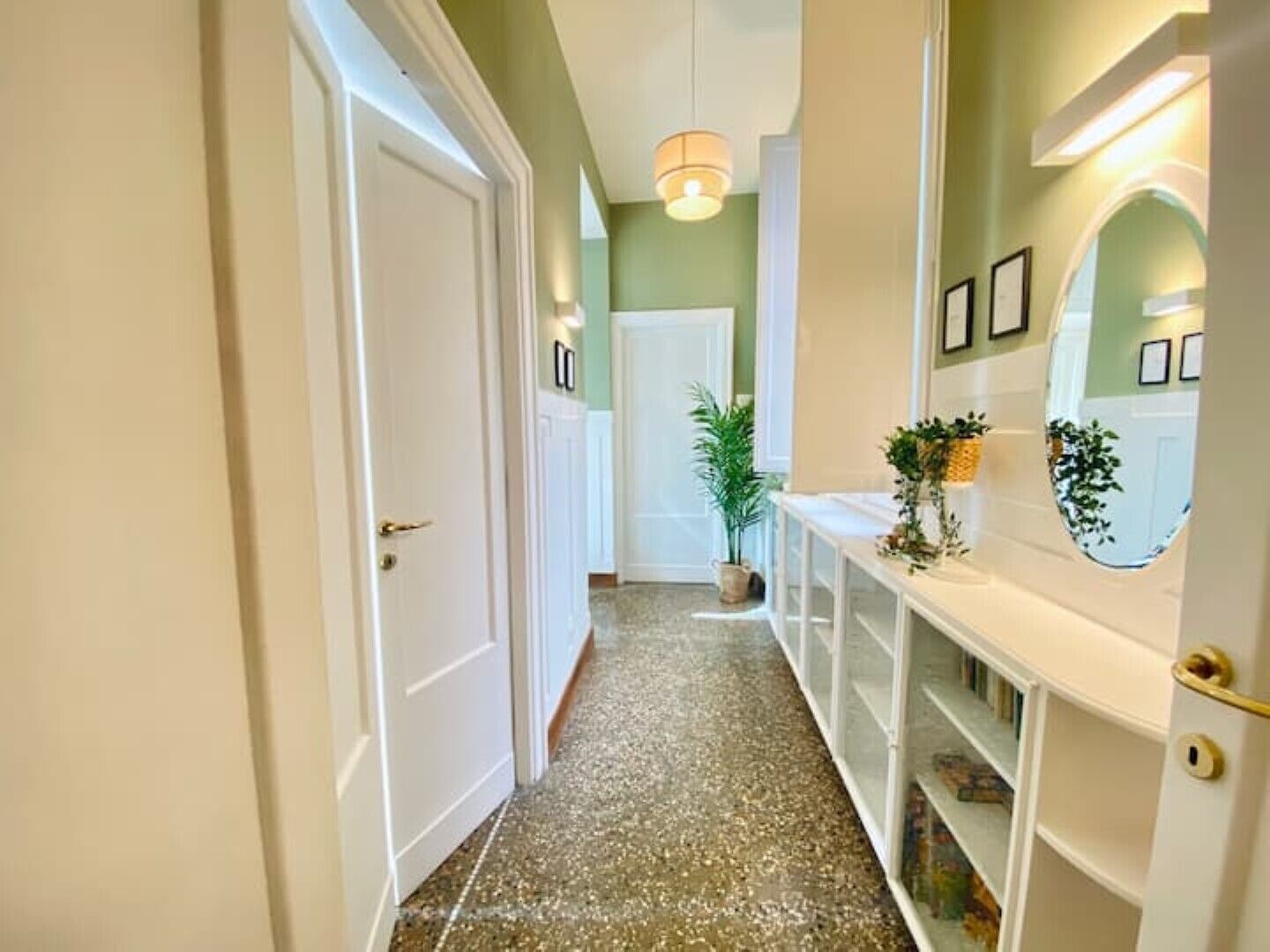 A hallway with a white door, a plant, and a white console table with a mirror.