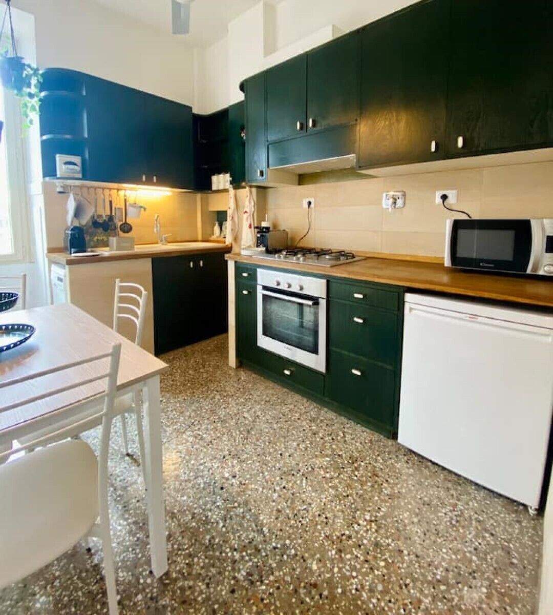 Una cocina compacta con armarios verde oscuro, una encimera blanca, horno empotrado, microondas y lavavajillas.