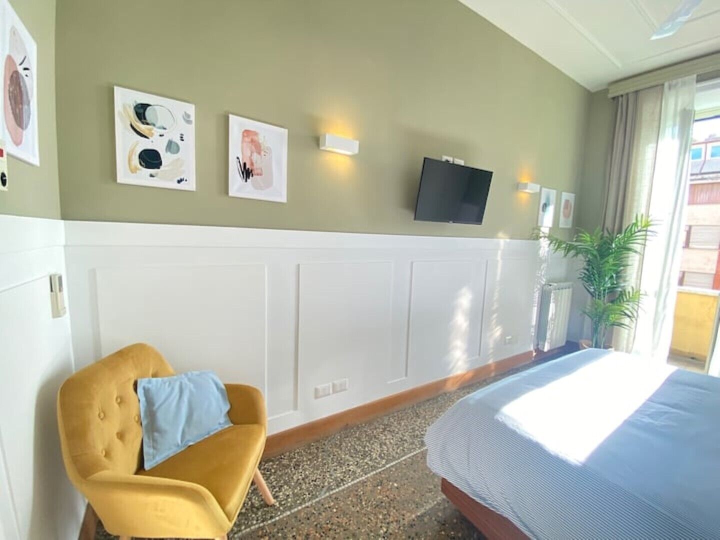 Een hotelkamer met een bed, een gele fauteuil, een flatscreen televisie aan de muur en kunstwerken aan de wand.