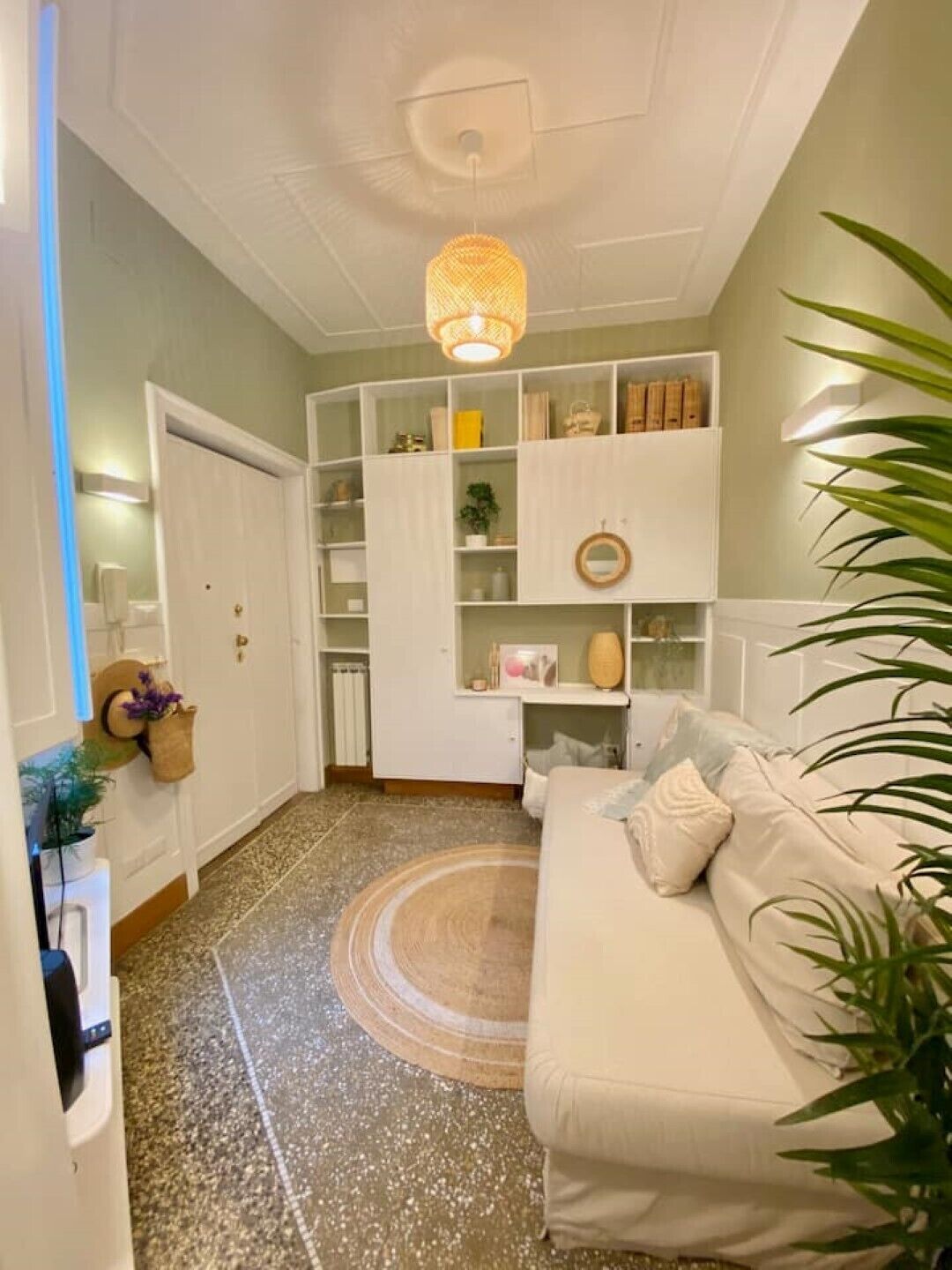 A hallway with a white door, a white sofa, and a shelving unit with various items.