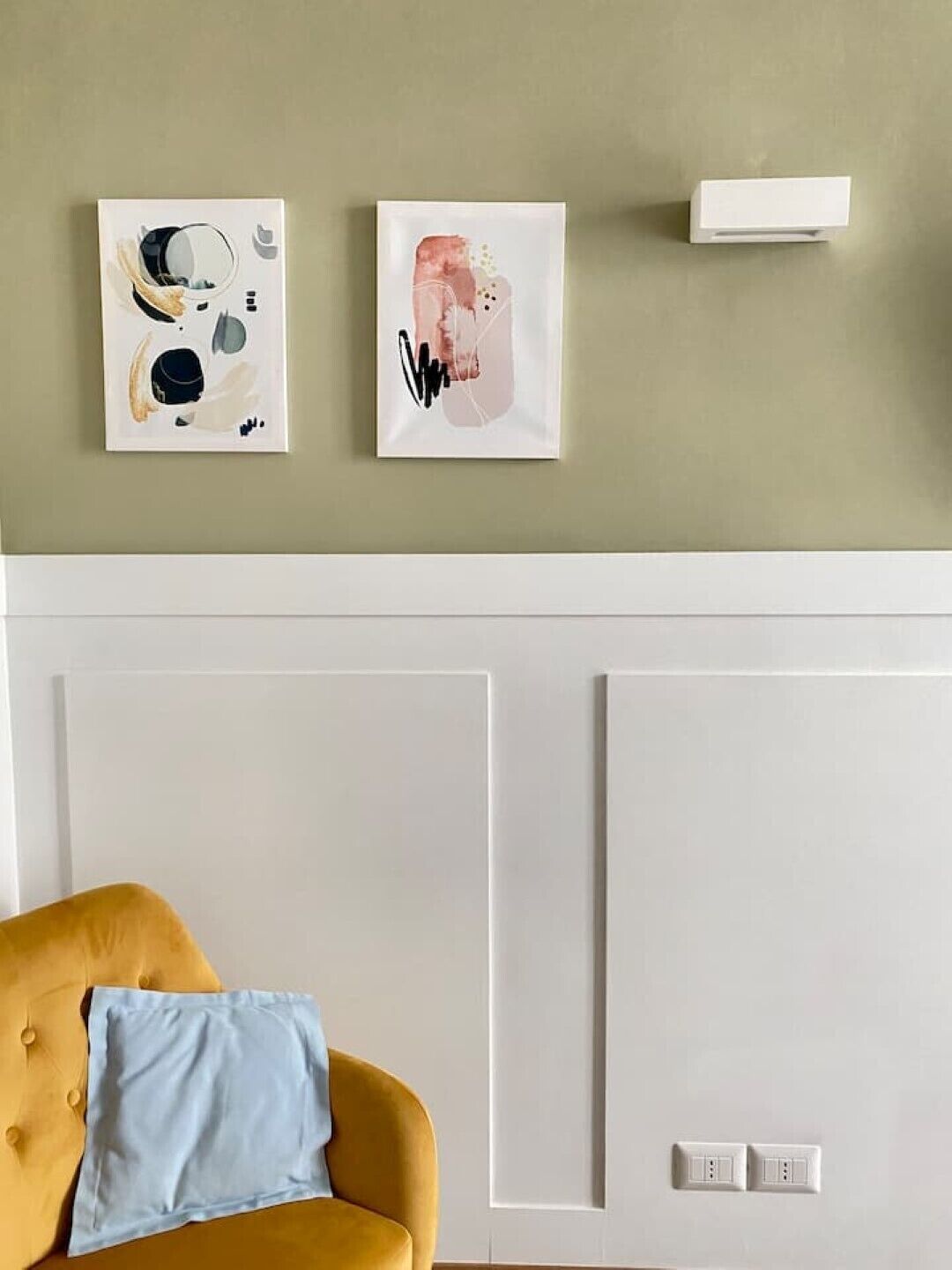A room with a yellow sofa, a light blue pillow, and two wall-mounted artworks.