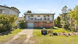 A two-story house with a front yard, a driveway, and a sign in the front yard. - Baxter's Beach House by Experience Jervis Bay (Vincentia)
