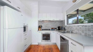 A modern kitchen with white cabinetry, a tiled backsplash, and a wooden floor. - Baxter's Beach House by Experience Jervis Bay (Vincentia)