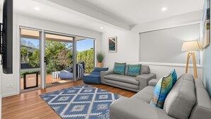 A modern living room with a grey sofa, blue and white patterned rug, and a view of a garden through glass doors. - Baxter's Beach House by Experience Jervis Bay (Vincentia)