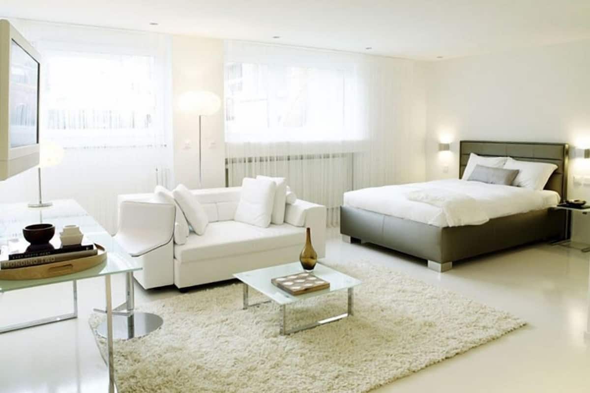Une chambre à coucher moderne et bien éclairée, avec un canapé blanc, un lit et une table basse.