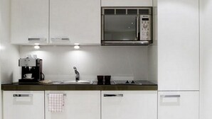 Una cocina moderna con gabinetes blancos, un microondas de acero inoxidable, una cafetera y un lavamanos.