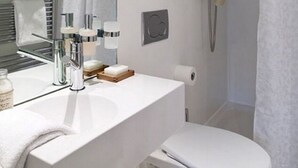 Un baño moderno con un lavamanos blanco, espejo e inodoro. Cuenta con una ducha con cabezal de mano y cortina.