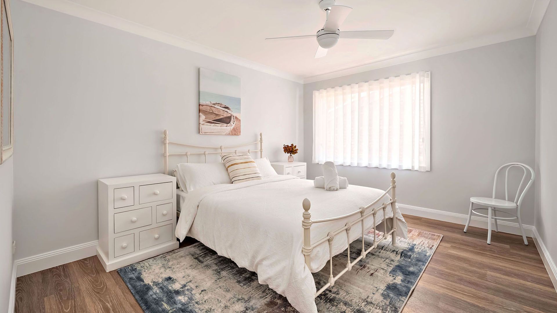 A bedroom with a bed, a nightstand, a chair, and a ceiling fan.
