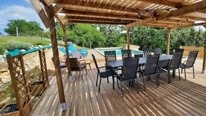 Eine Holzterrasse mit Pool, Sitzgelegenheiten im Freien und einer Pergola.