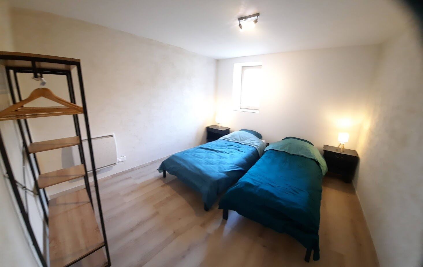 Ein kleiner, gut beleuchteter Raum mit zwei Einzelbetten, einem Holzschrank und einem Fenster, das für natürliches Licht sorgt.