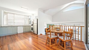 Een moderne keuken met witte kasten, een eethoek met houten stoelen en grote ramen.