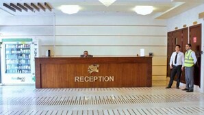 Un mostrador de recepción con un letrero que dice "RECEPTION" y un logotipo arriba. Dos personas están de pie a la derecha del mostrador.