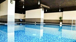 Una piscina interior con agua cristalina, paredes de azulejos e iluminación en el techo.