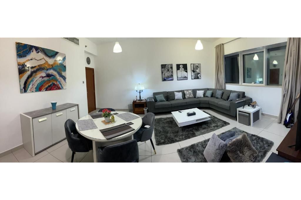 Un salon moderne avec un canapé d’angle gris, une table à manger avec des chaises, une table basse et un grand tableau abstrait accroché au mur.