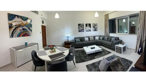 Una sala de estar moderna con un sofá seccional gris, una mesa de comedor con sillas, una mesa de centro y un cuadro abstracto grande en la pared.