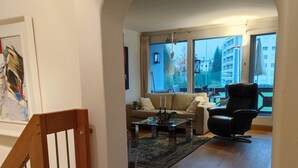 A spacious living room with a wooden staircase, a sofa, a coffee table, and a black chair.