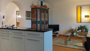 A modern kitchen with a central island, a dining area with a table and chairs, and a living room with a sofa and a TV.
