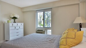 A bedroom with a bed, a dresser, a window with a view, and a lamp. - Harvard Square! (Cambridge)
