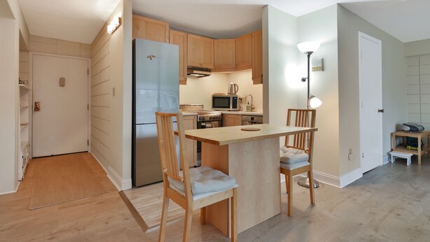 A compact kitchen with wooden cabinets, a refrigerator, a microwave, and a small dining area with two chairs. - Harvard Square! (Cambridge)
