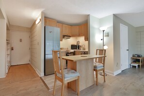 A compact kitchen with wooden cabinets, a refrigerator, a microwave, and a small dining area with two chairs. - Harvard Square! (Cambridge)