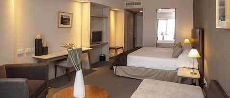 Una habitación de hotel con una cama, un escritorio, una silla, una mesita y una lámpara.