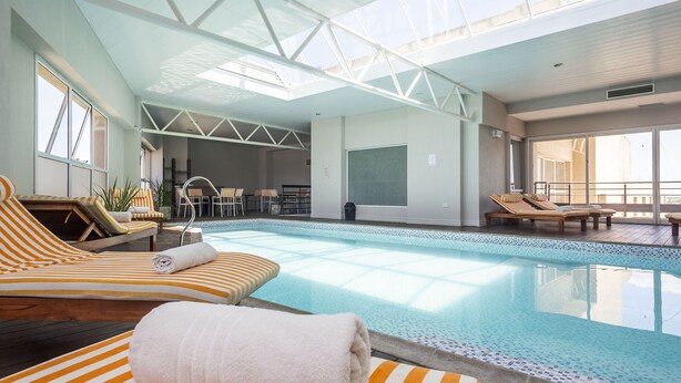 A modern indoor pool area with sun loungers and a clear view of the pool. - Visit Hotel & Apart (San Luis)