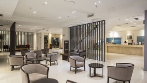 A modern hotel lobby with a seating area, a reception desk, and a staircase. - Visit Hotel & Apart (San Luis)
