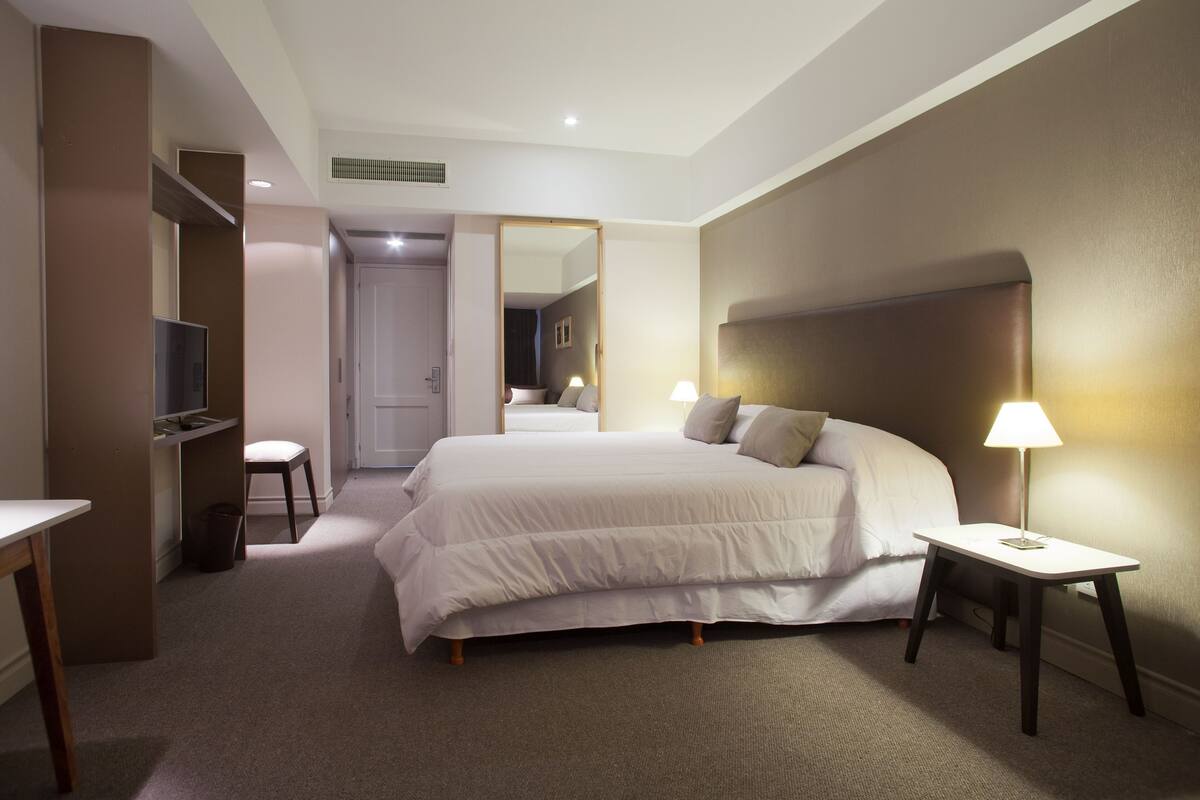 A hotel room with a large bed, bedside tables, a TV, and a mirror.
