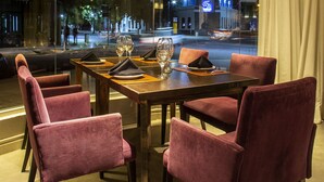 A dining area with a glass wall, a round table, and red upholstered chairs. - Visit Hotel & Apart (San Luis)