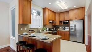 A modern kitchen with wooden cabinets, stainless steel appliances, and a central island with stools. - Refined 3BR Retreat in the Heart of Inner Richmond, Near Presidio, Golden Gate Park & Clement Street (San Francisco)