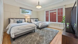 A bedroom with two beds, a large window with red shutters, a ceiling light, and a small plant on a console table. - Serene Inner Richmond 3BR Retreat Near Golden Gate Park, Clement Street & Geary Blvd (San Francisco)