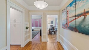 A hallway with wooden flooring, white cabinetry, and a large painting of a bridge. - Serene Inner Richmond 3BR Retreat Near Golden Gate Park, Clement Street & Geary Blvd (San Francisco)