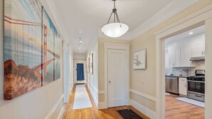 A hallway with wooden flooring, a white door, and a kitchen area with stainless steel appliances. - Serene Inner Richmond 3BR Retreat Near Golden Gate Park, Clement Street & Geary Blvd (San Francisco)