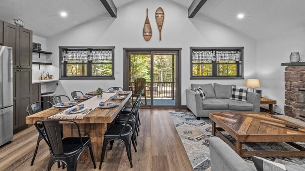 A spacious kitchen with a dining area, a fireplace, and a large window overlooking a forested area.