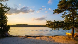 A beach with a wooden dock, picnic table, and a sandy area with trees.