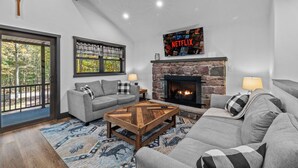 A modern living room with a fireplace, a grey sofa, a coffee table, and a large TV screen displaying the Netflix logo.