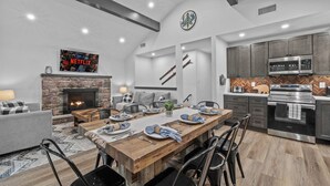 A modern kitchen with stainless steel appliances, a dining area with a wooden table, and a cozy fireplace.