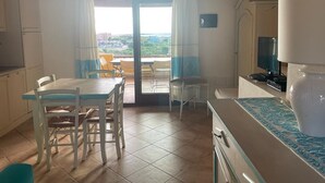 Une cuisine avec une table et des chaises, un téléviseur et une vue sur l’extérieur, visible à travers une porte vitrée.