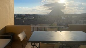 Un balcon avec une table et des chaises, donnant sur une ville et offrant une vue sur une colline imposante au loin.