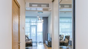 A modern hallway leading to a living area with a large window, a flat-screen TV, and a seating area with a sofa and chairs. - Fresh and lovely apartment (Jurmala)