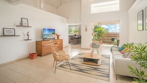 Uma sala de estar ampla com uma TV grande, cadeiras de vime, um armário de madeira e vista para o exterior.