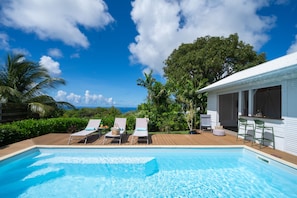 A pool area with lounge chairs and a view of the ocean.
