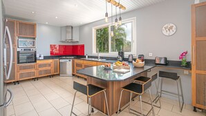 Uma cozinha moderna com uma ilha central, banquetas, uma janela grande e vista para o verde lá fora.