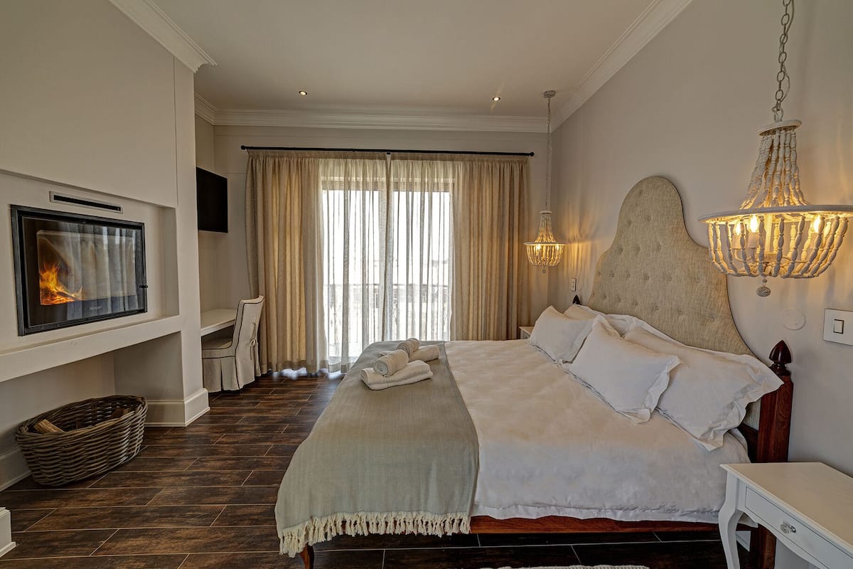 A bedroom with a bed, a fireplace, a desk, and a large window with curtains.