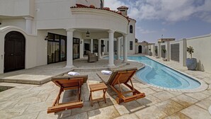 A poolside area with two wooden lounge chairs, a covered seating area, and a swimming pool. - Lagoon Suites Boutique Hotel (Walvis Bay)